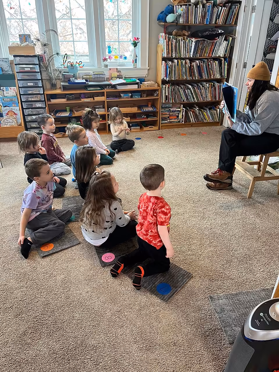 Elementary students seated on floor mats listening to a visiting Annett Nature Center educator