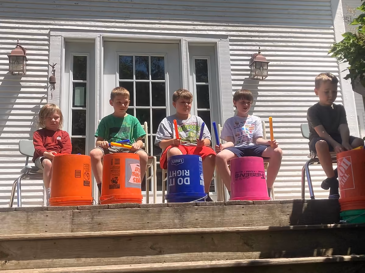 Five Main Street School students performing outside with drumsticks and colorful buckets