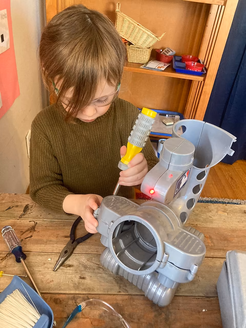 Student wearing safety glasses using a screwdriver to take apart a plastic machine at a worktable